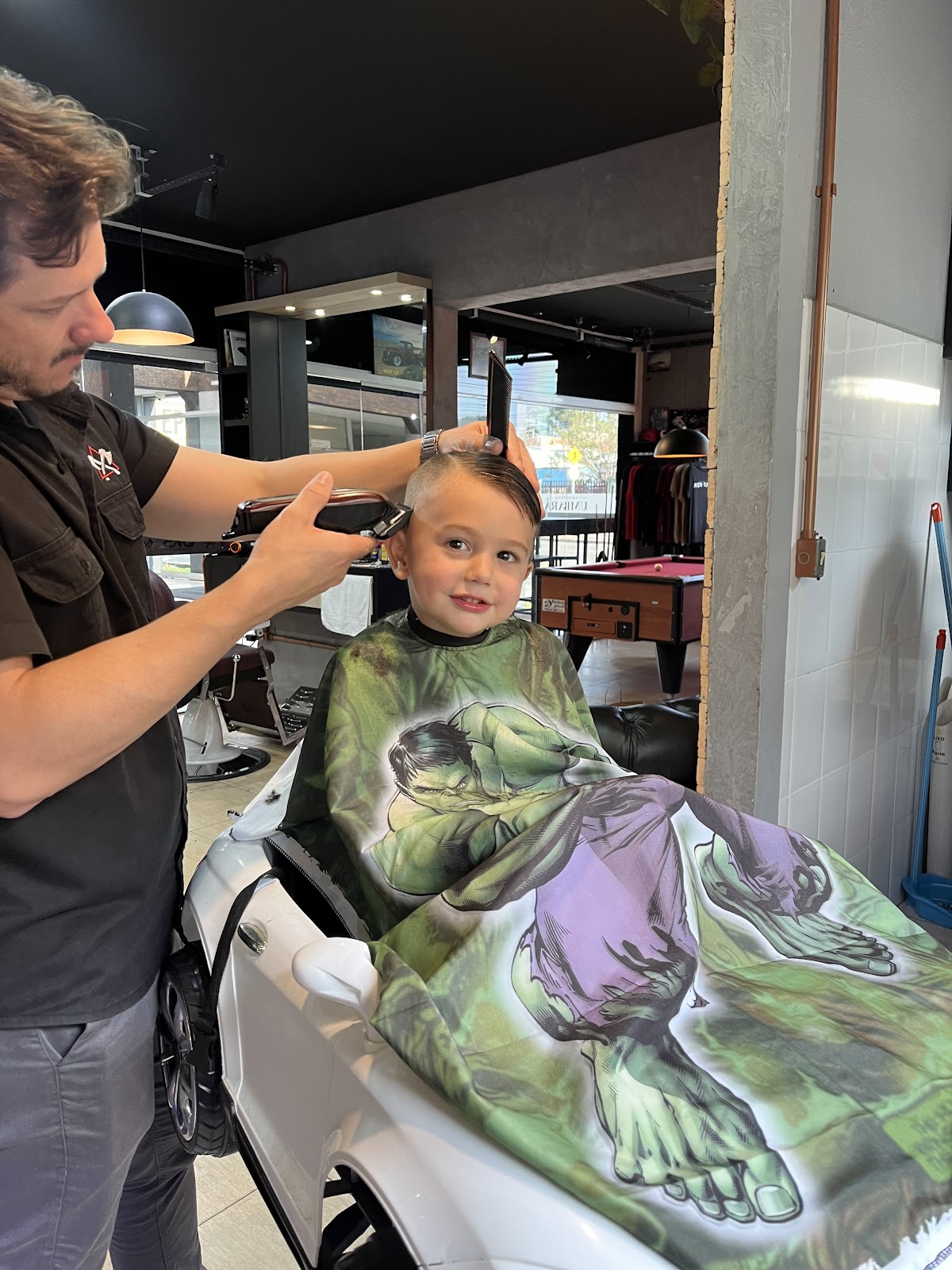 Barbeiro cortando o cabelo de uma criança dentro da Øks Barbearia - Pub